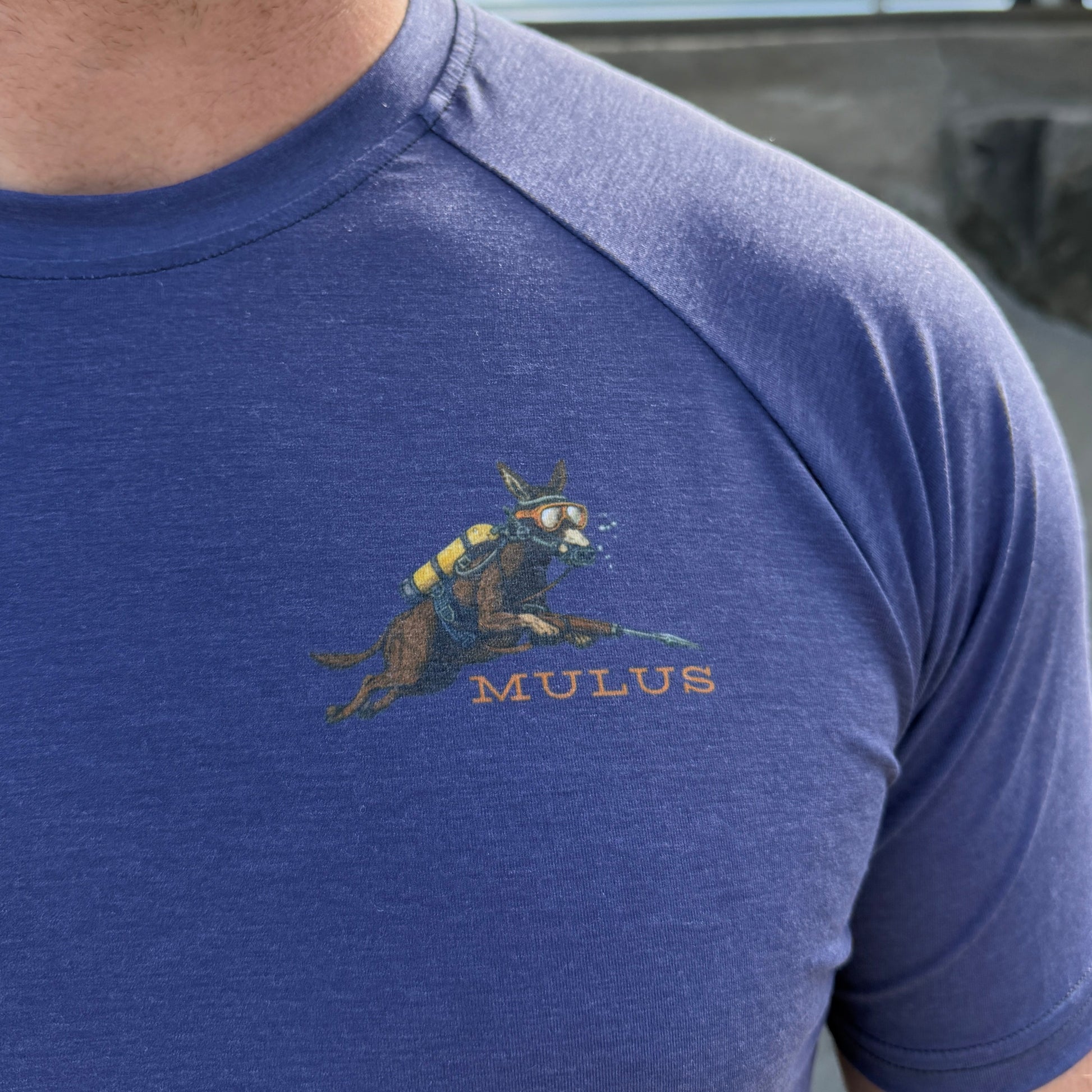Close-up of a person wearing a blue shirt with a logo, standing outdoors.