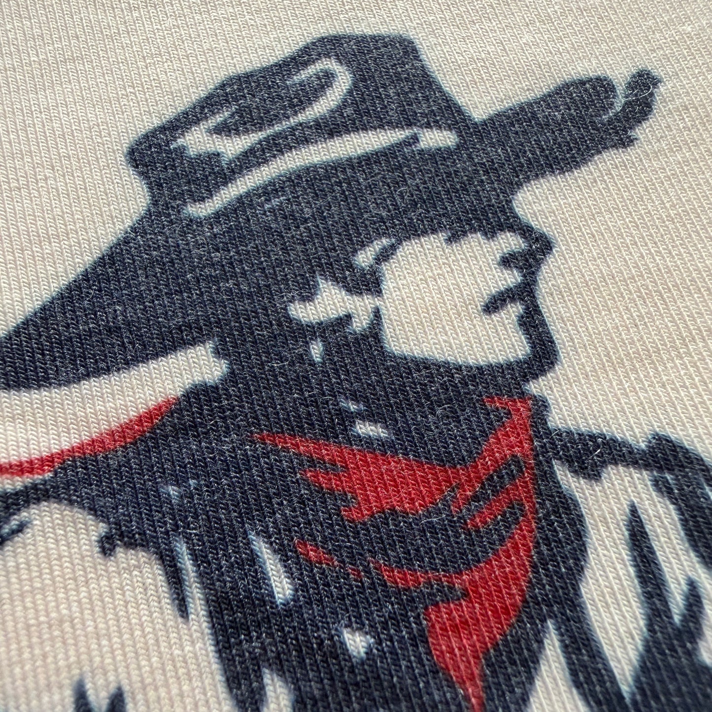 Close-up of a printed textile pattern featuring a stylized face and hair in dark navy and red on a light beige fabric background.