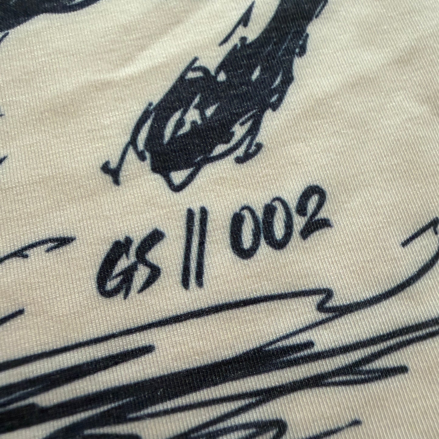 Close-up of a cream-colored fabric surface printed with a black graphic illustration and the text GS || 002'.
