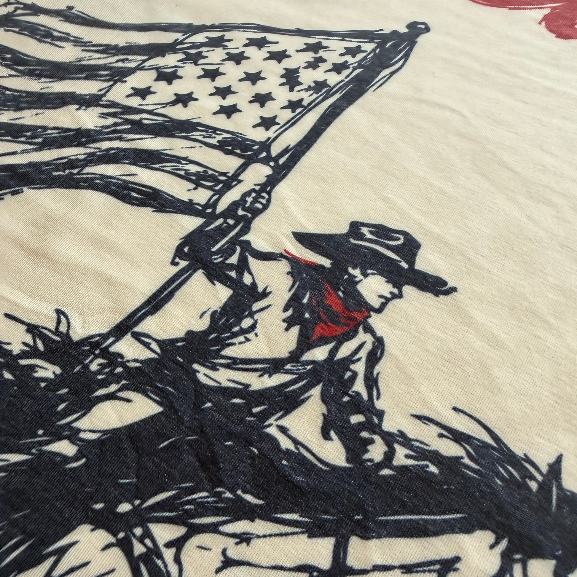 A close-up of a cream-colored fabric featuring a black ink sketch of a cowboy holding a tattered American flag, with a small red accent near the hat.