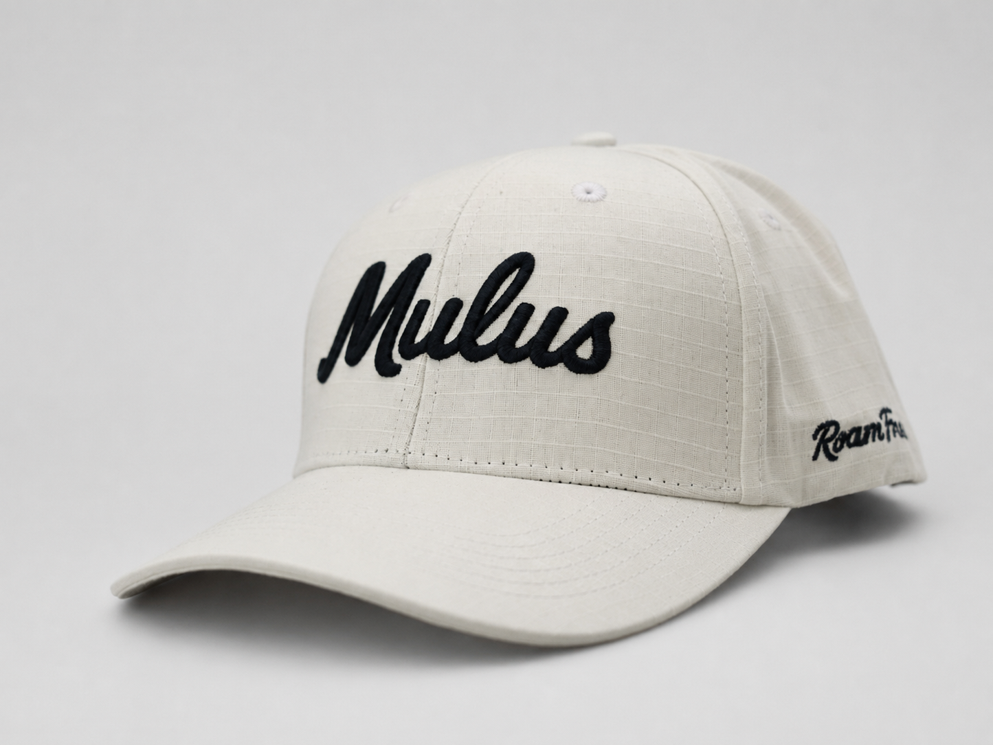 An off-white baseball cap with 'Mulus' embroidered in black script on the front and 'RoamFree' on the side, shown against a light gray background.